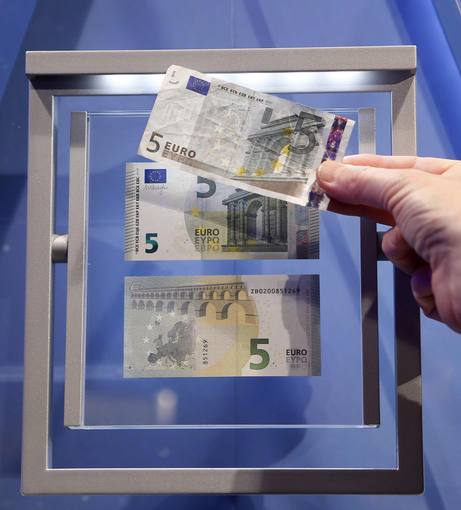 A journalist compares the new 5 euro note with an old one (top) during a ceremony with Draghi, President of the European Central Bank (ECB), in Frankfurt
