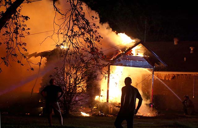 A person looks on as emergency workers fight a house fire