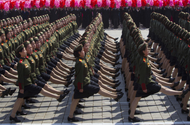 North Korean soldiers march in front of flower waving civilians durin