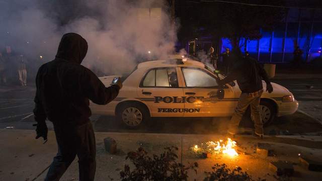 Men photograph a burning police vehicle after it was damaged and set ablaze by protesters outside of City Hall in Ferguson