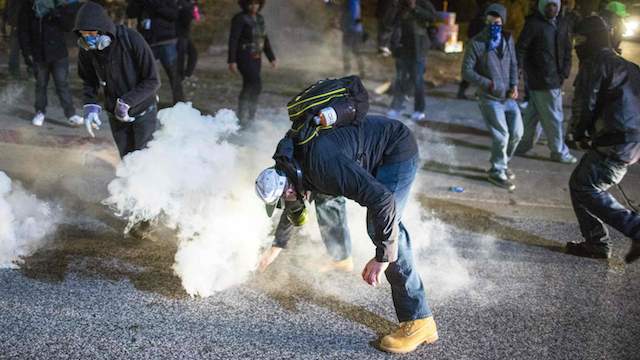 A protester reaches for a tear gas canister during a second night of protests in Ferguson, Missouri