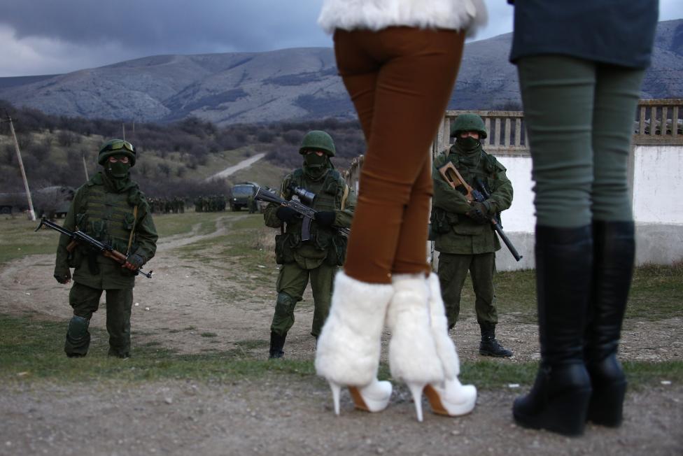 Local women watch armed men, believed to be Russian soldiers, assemble near a Ukrainian military base in Perevalnoe