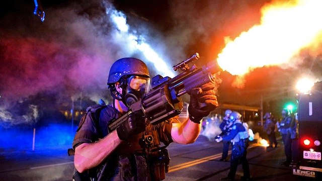 A member of the St. Louis County Police tactical team fires tear gas into a crowd of people in response to a series of gunshots fired at police during demonstrations in Ferguson, Missouri