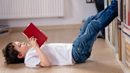 Niño acostado en el suelo leyendo un libro.