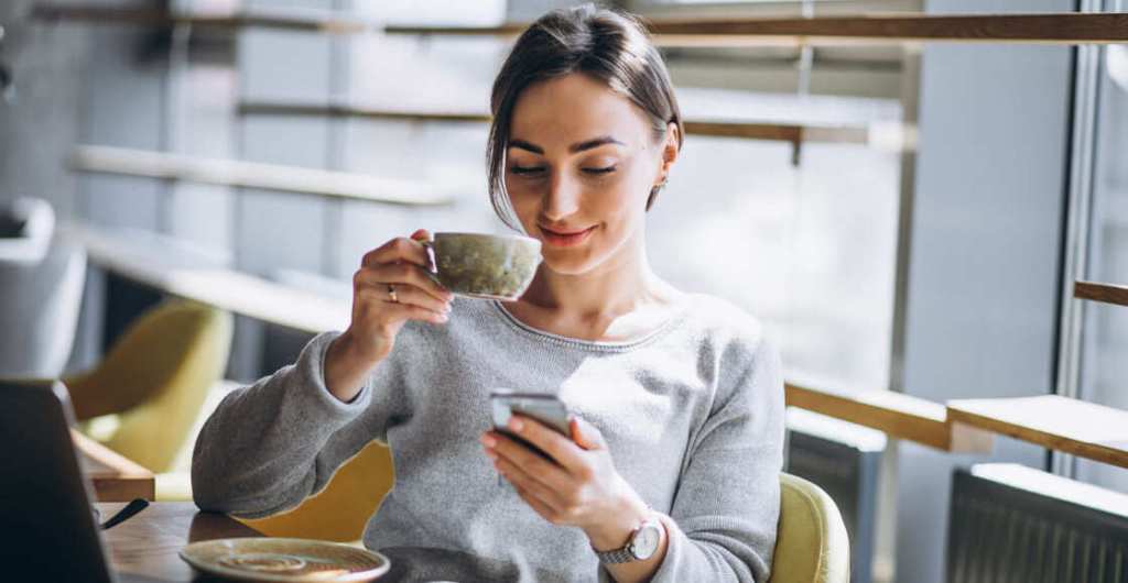 Mujer sentada tomando café y usando smartphone