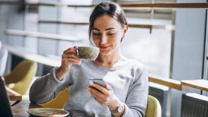 Mujer sentada tomando café y usando smartphone