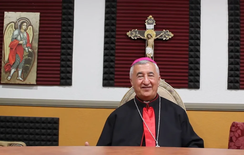 Emanuel Shaleta sentado frente a símbolos religiosos en una imagen de la Eparquía Caldea de San Pedro Apóstol de San Diego.