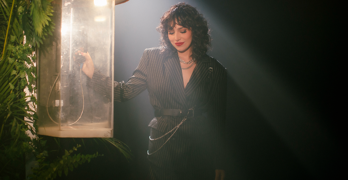 Cantante dentro de una cabina telefónica vintage iluminada, con traje negro a rayas y estilo cinematográfico.