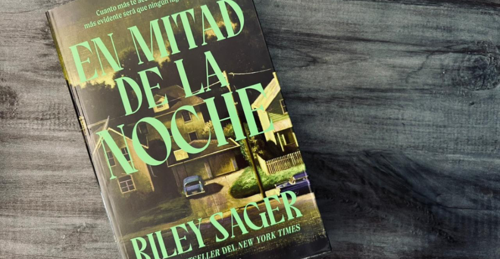 Portada del libro En mitad de la noche de Riley Sager sobre una mesa de madera.