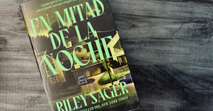 Portada del libro En mitad de la noche de Riley Sager sobre una mesa de madera.