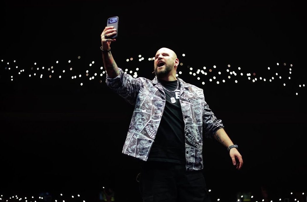 El Temach sosteniendo un teléfono celular durante una presentación ante el público.