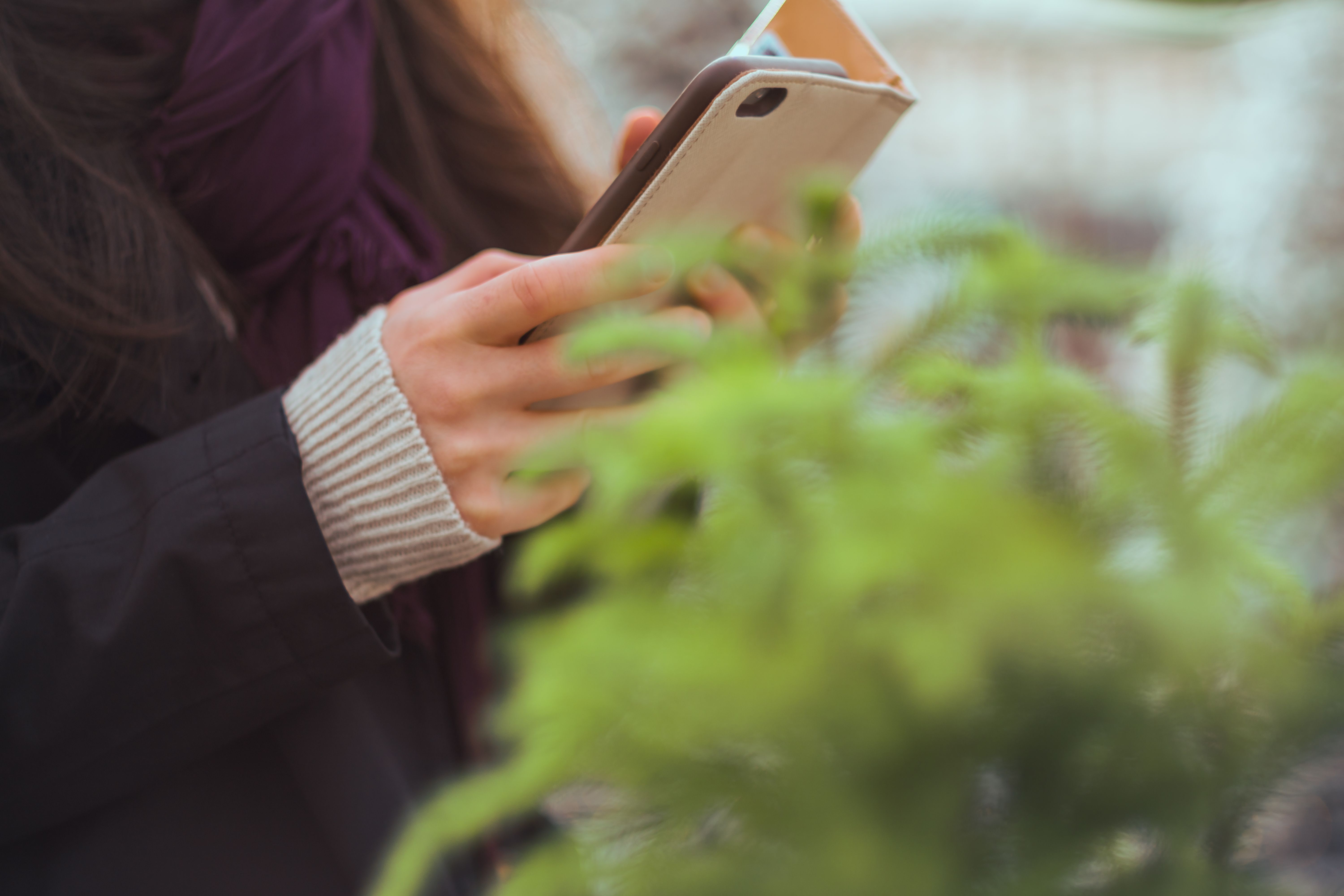 Persona usando un teléfono celular mientras navega por internet en un espacio al aire libre.