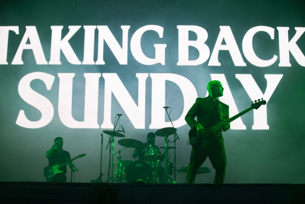 Taking Back Sunday tocando en vivo en el escenario con luces verdes y su logo de fondo durante el Vans Warped Tour CDMX 2026.