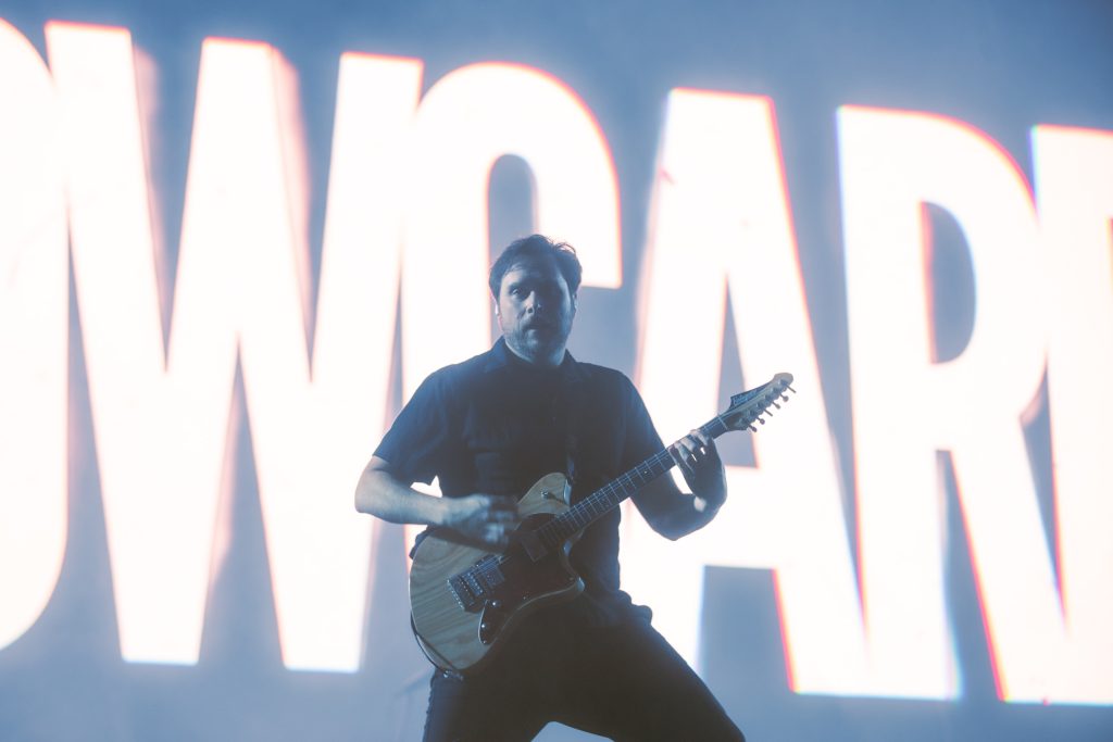 Integrante de Yellowcard tocando la guitarra en vivo con el logo de la banda proyectado al fondo en el Vans Warped Tour CDMX 2026.