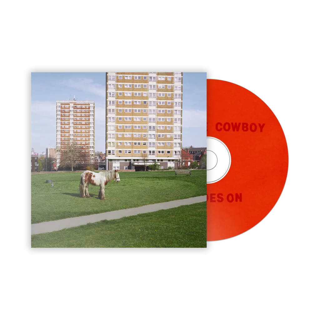 Portada del disco físico 'It Goes On' de la banda Westside Cowboy, mostrando un caballo de pastoreo frente a dos edificios habitacionales y un CD color naranja.