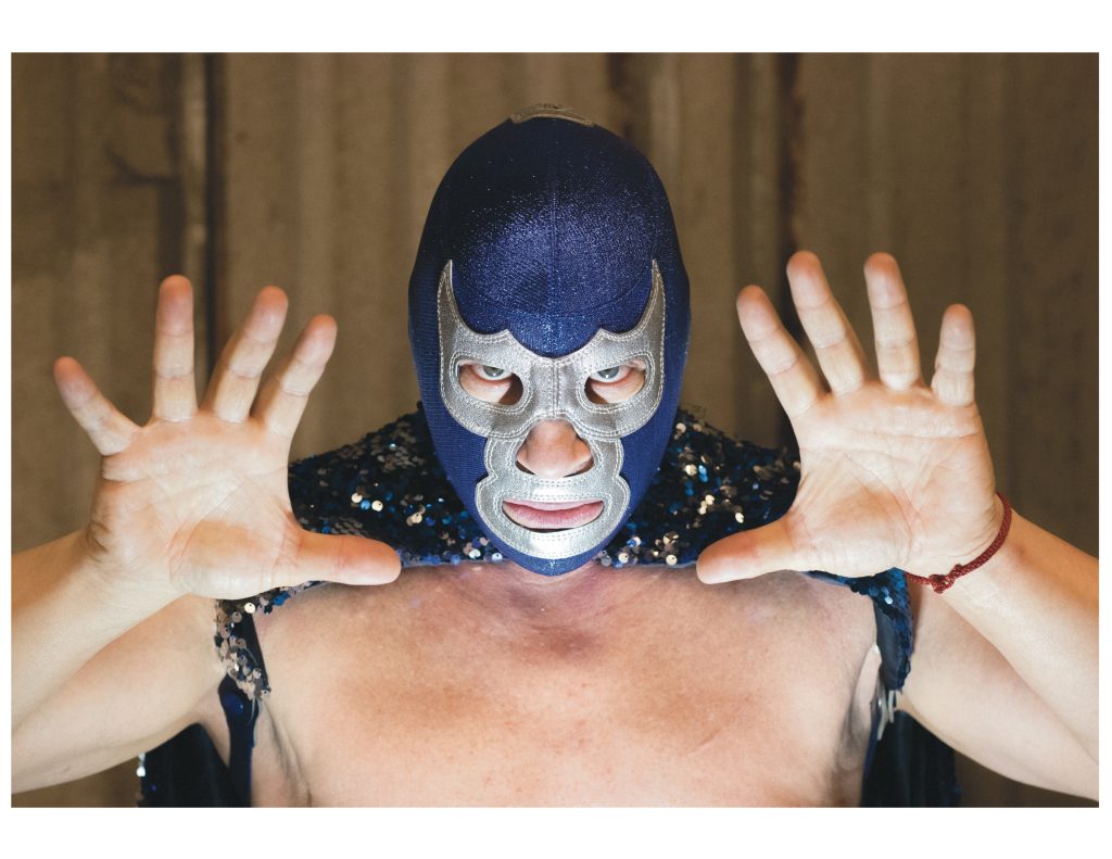El luchador Blue Demon Jr. posando con las manos abiertas hacia la cámara, usando su característica máscara azul.